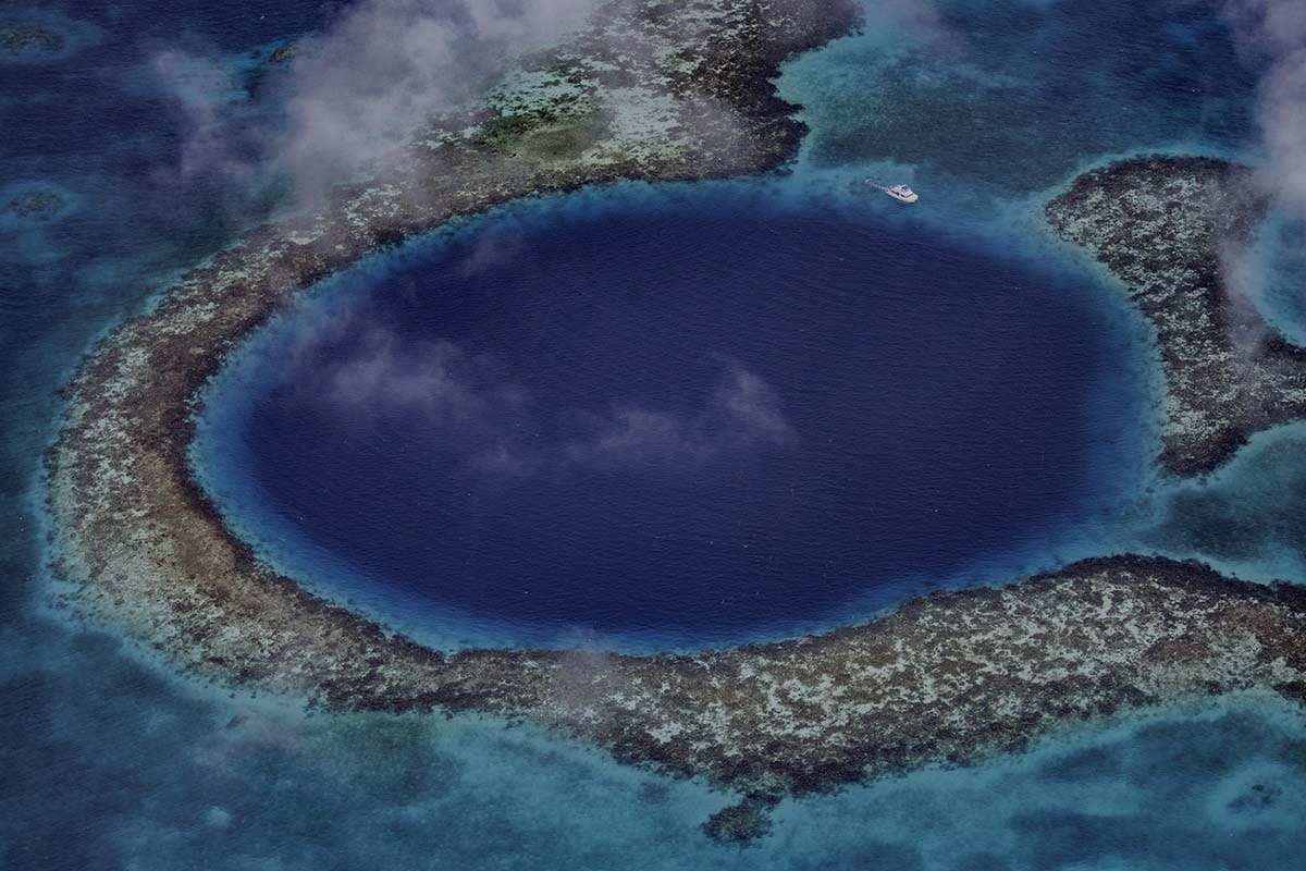 Aerial shot of a coral reef surrounding a deep blue area of water -Is Belize good for solo travel